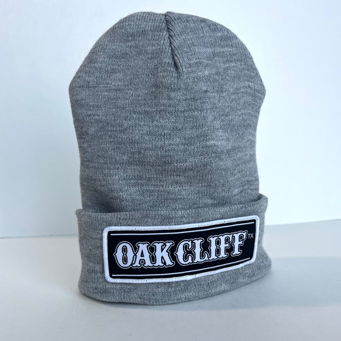 Side view of the Oak Cliff Beanie featuring a gray knit and a distinctive patch. This stylish accessory is a fantastic Texas themed gift, representing Texas Made Gifts, suitable for anyone seeking souvenirs from Texas or a memorable Dallas souvenir.