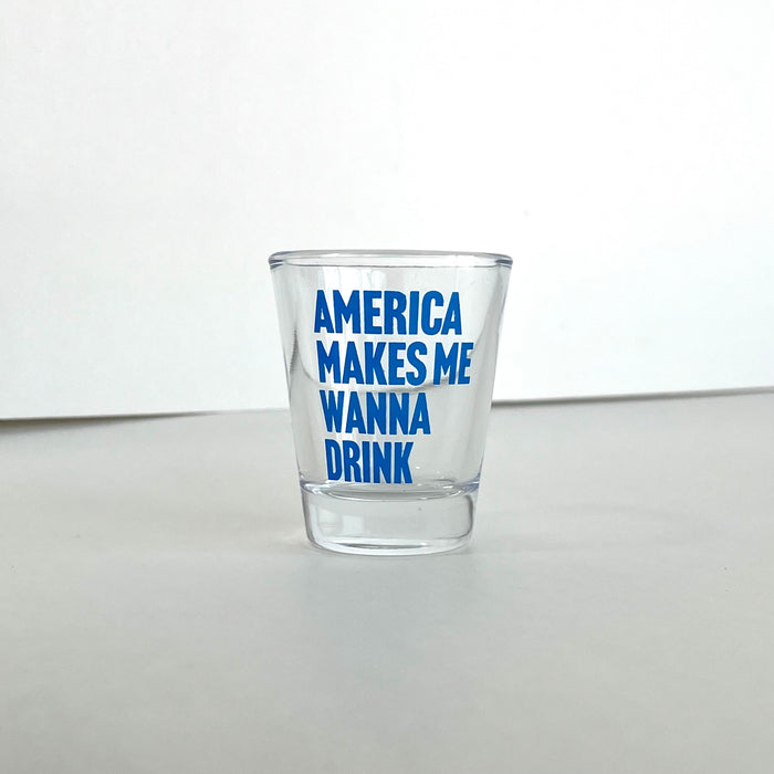 America Makes Me Wanna Drink Shot Glass, a clear glass shot glass featuring bold blue text, perfect as a Texas themed gift or for anyone looking for Texas Made Gifts. This Dallas souvenir is an ideal choice for Texan gifts.