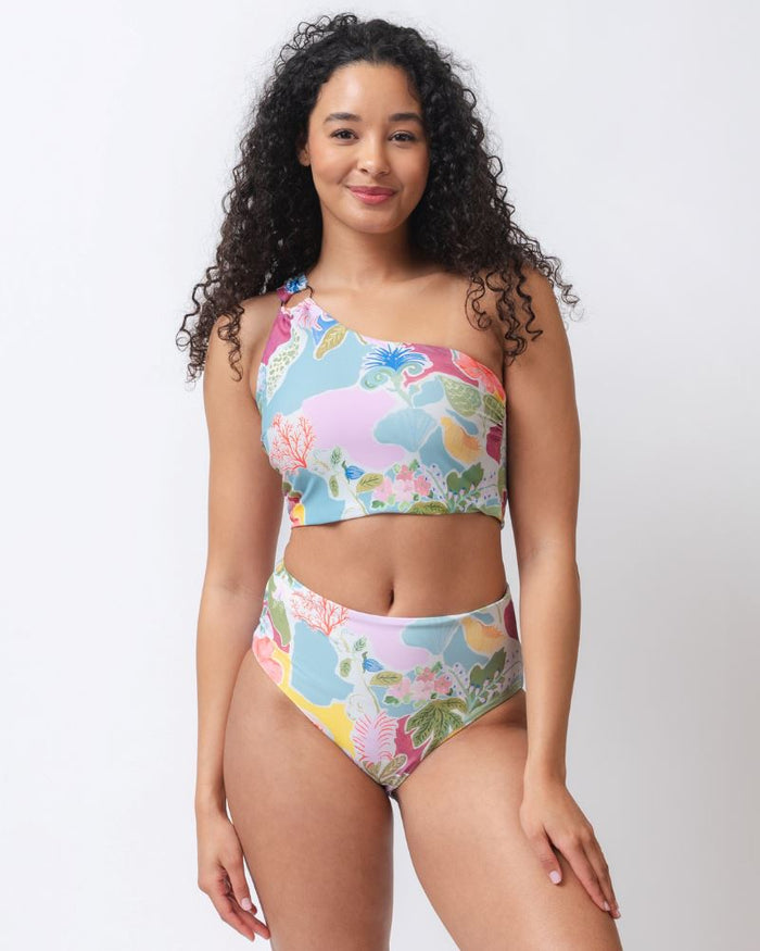 Photo of a woman wearing a colorful seashell inspired high waist swim bottom and a colorful seashell inspired one-shoulder swim crop top