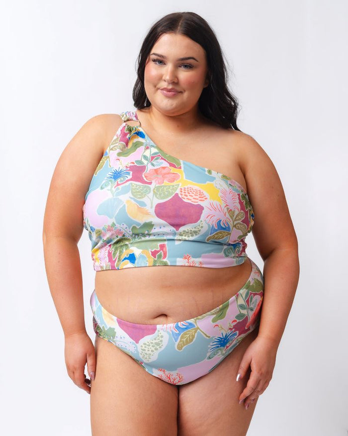 Photo of a woman wearing a colorful seashell inspired high waist swim bottom and a colorful seashell inspired one-shoulder swim crop top