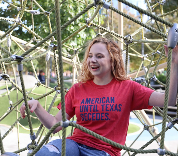 Person wearing an 'American until Texas Seceds' t-shirt on a playground.structure