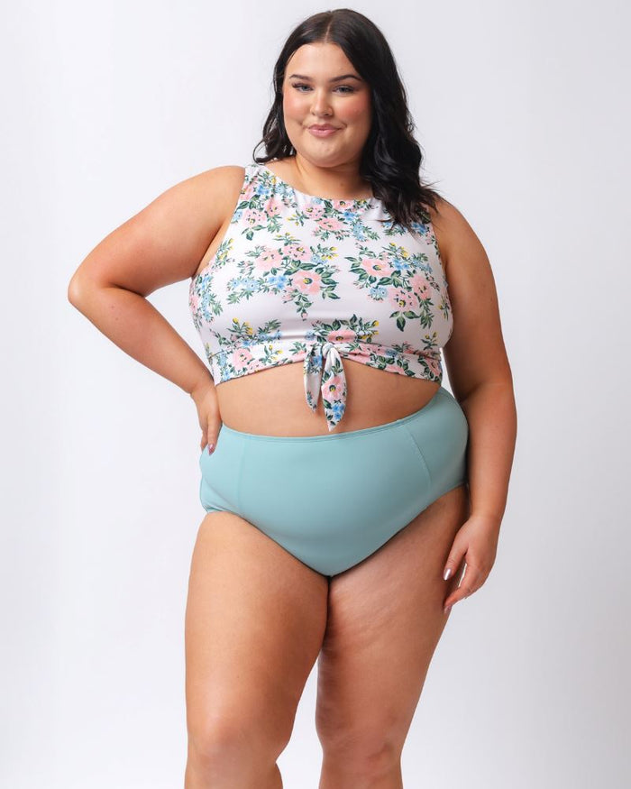 Photo of a woman wearing a light blue high waist swim bottom and a pink and white floral swim crop top