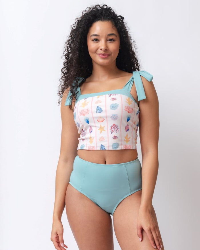Photo of a woman wearing a light blue high waist swim bottom and a seashell striped shoulder-tie swim crop top