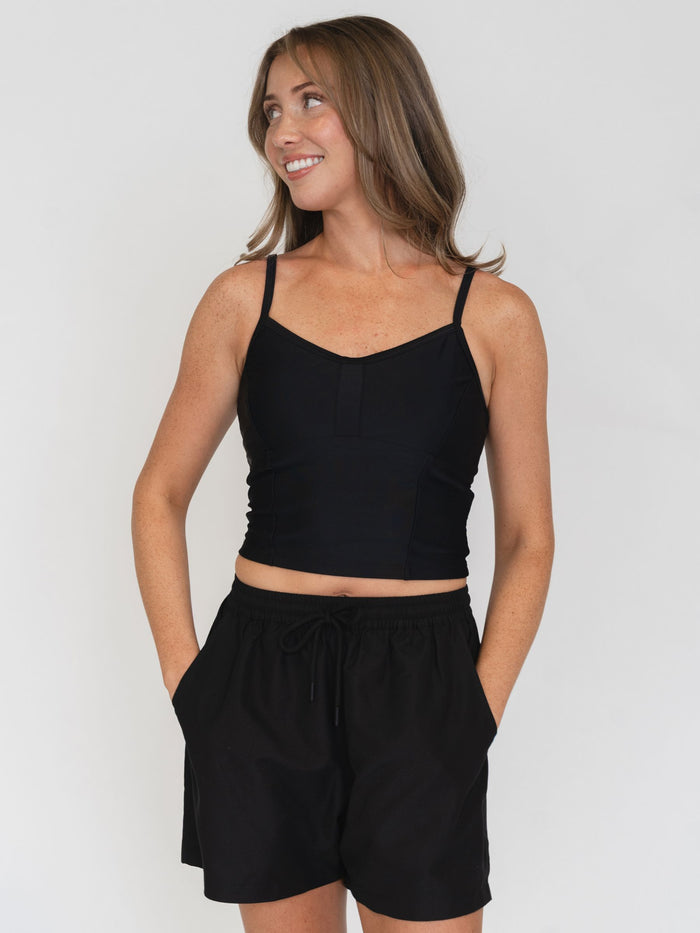 Woman wearing a black tank top and black shorts on a white background