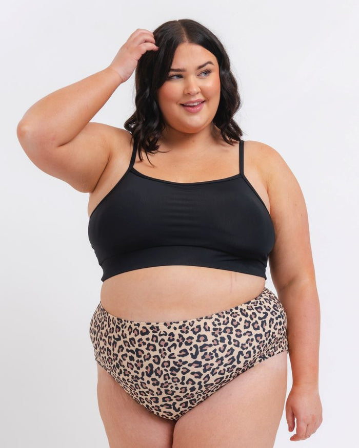 woman wearing a black Sports bra and leopard bikini bottoms on a white background