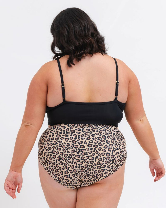 woman wearing a black sports bra and a leopard bikini bottom on a white background from behind