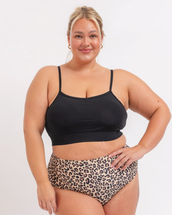 woman wearing Black sports bra with leopard bikini bottoms on a white background