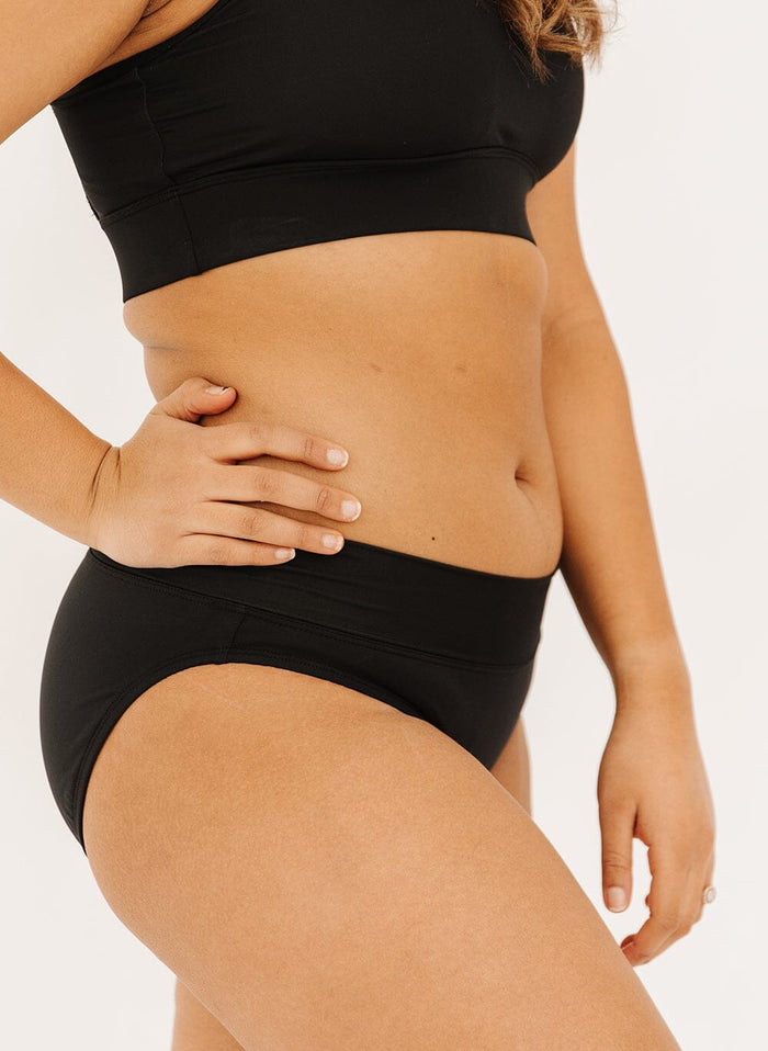 Photo of a woman in a black classic swim bottoms and top, side angle