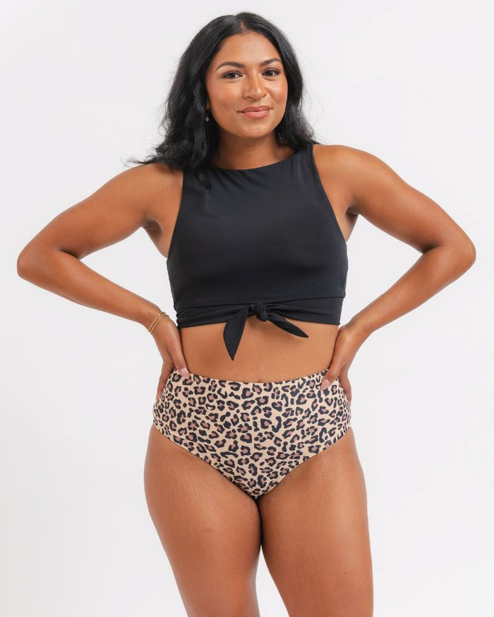 A woman modeling a two-piece swimsuit with a black halter crop top and high-waisted leopard print bikini bottoms, posed against a white background.