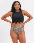 A woman modeling a two-piece swimsuit with a black halter crop top and high-waisted leopard print bikini bottoms, posed against a white background.