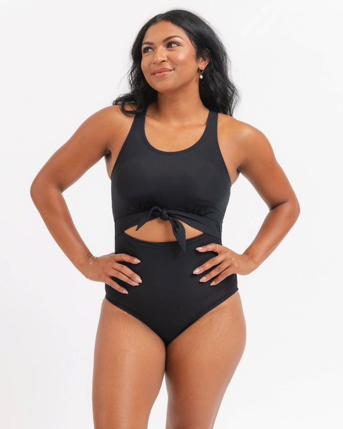 Woman wearing a black knotted one piece swimsuit with a white background