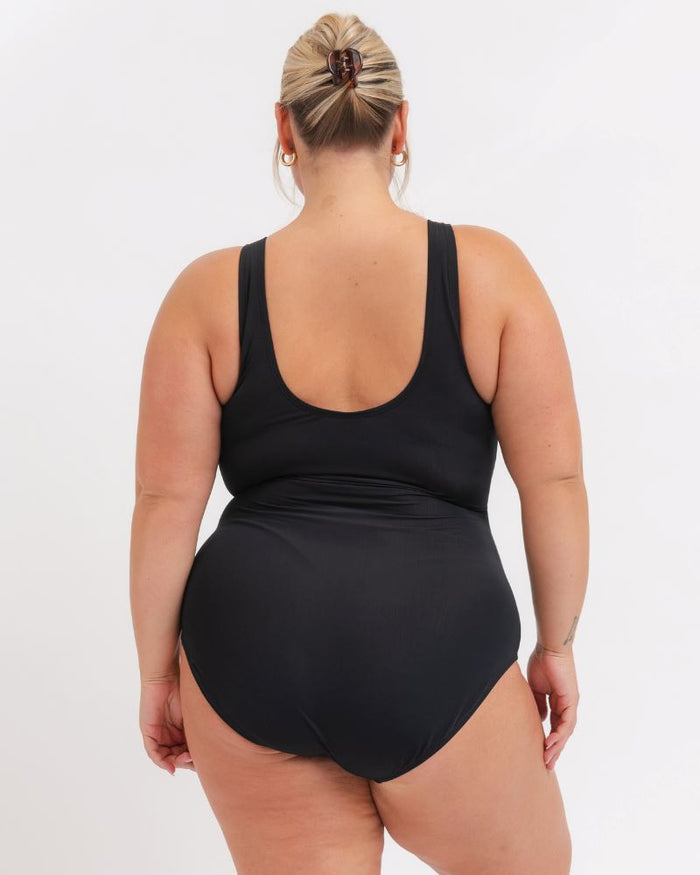 back view of a woman wearing a black knotted one piece with a white background
