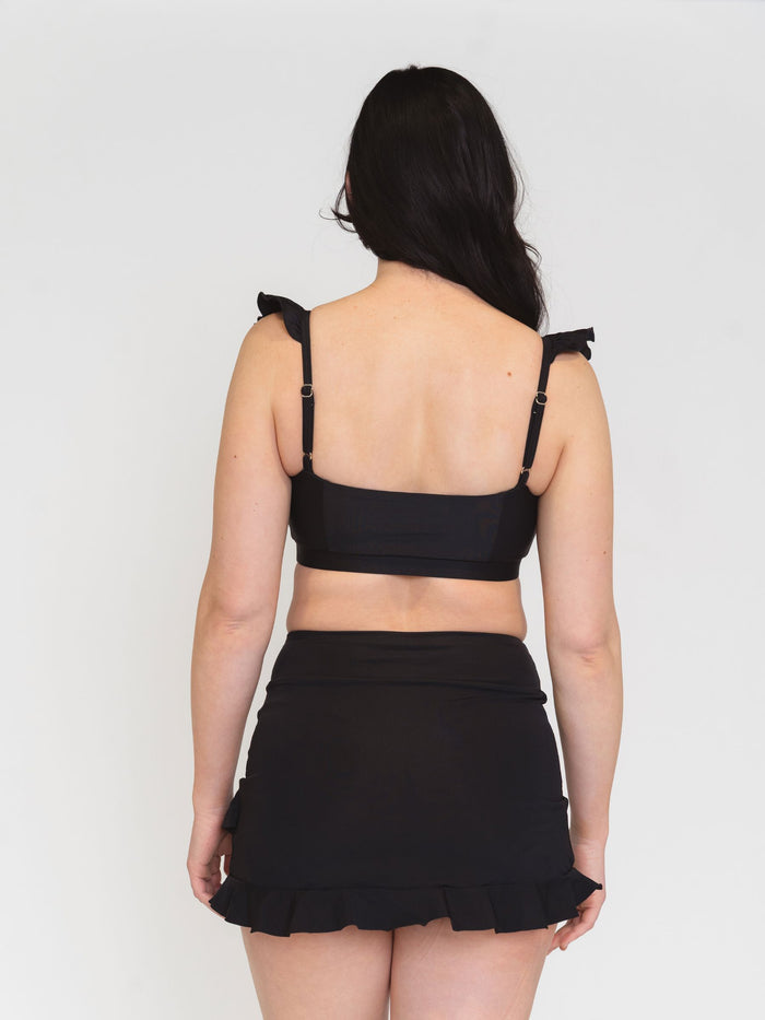 back view of a model wearing a black bikini set with ruffled straps on a white background