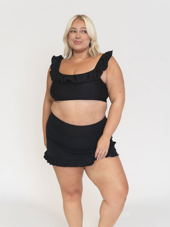 Woman wearing a black ruffled bikini and skirt against a white background