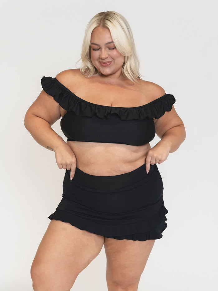 Woman wearing a black ruffle bikini top and skirt set on a white background
