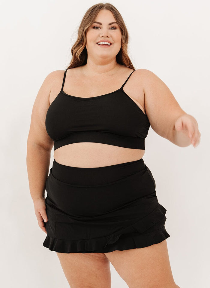 Photo of a woman wearing a black high-waist ruffle swim skirt with a black swim bralette.