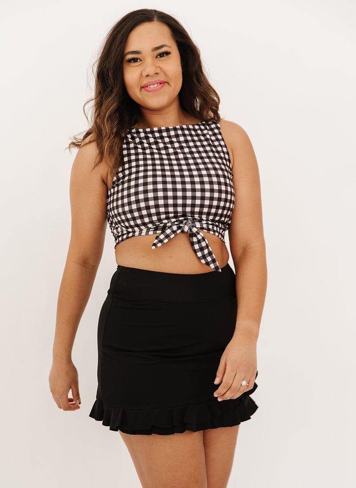 Photo of a woman wearing a black high-waist ruffle swim skirt with a black gingham knotted swim crop top.
