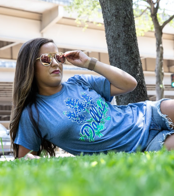 Photo of a woman wearing sunglasses and the Bullzerk Bluebonnets tshirt laying in the grass outside.