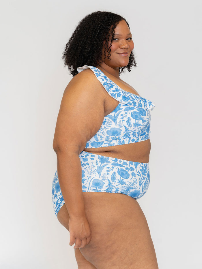 Side View of a Woman wearing a blue floral one-shoulder swimsuit against a white background