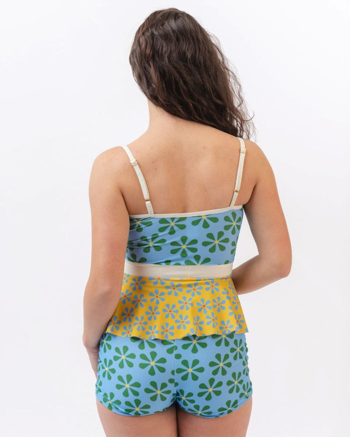 Photo of a woman wearing a multi-colored floral peplum swim top and a blue and green floral swim short bottom- back angle