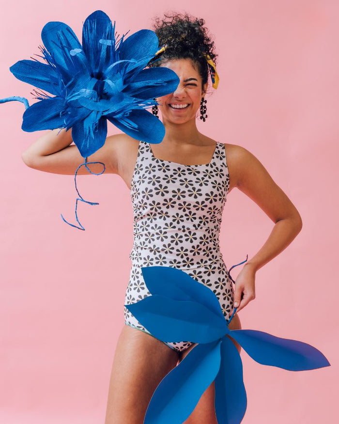 Photo of a woman posing with a large flower wearing a black and white floral square neck swim top and a black and white floral swim bottom