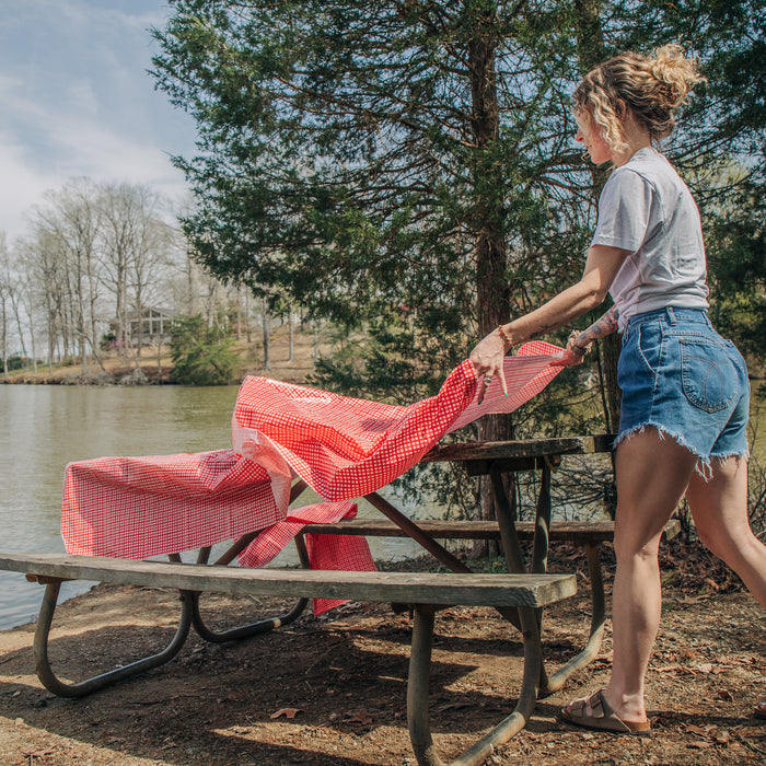 Camco 51019 Red Gingham Picnic Tablecloth Being Laid on Outdoor Table Lakeside | United RV Parts