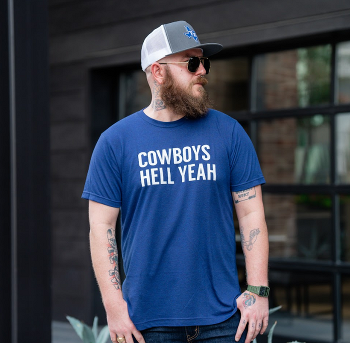 Photo of a man wearing the Bullzerk Cowboys Hell Yeah tshirt, sunglasses and a hat and looking off to the side.