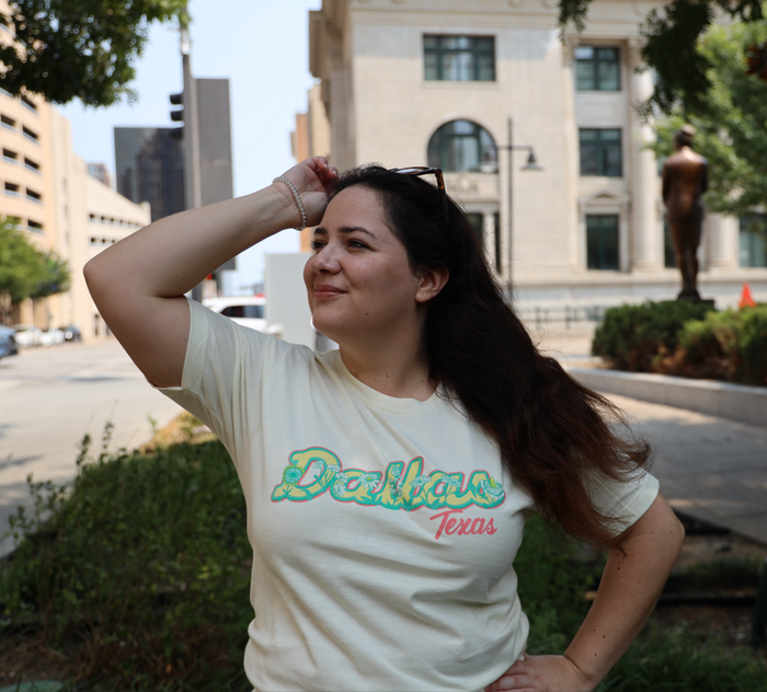 Woman wearing a Bullzerk Dallas Flowers t-shirt standing outdoors with a cityscape background