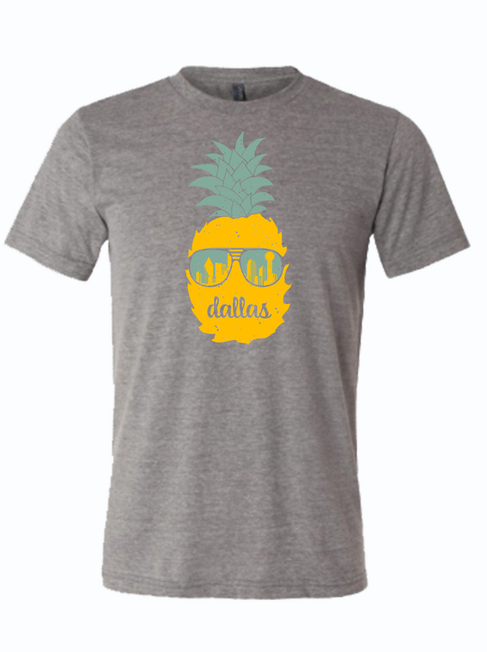 Gray t-shirt with a graphic design of a pineapple wearing sunglasses and 'dallas' text written on it.