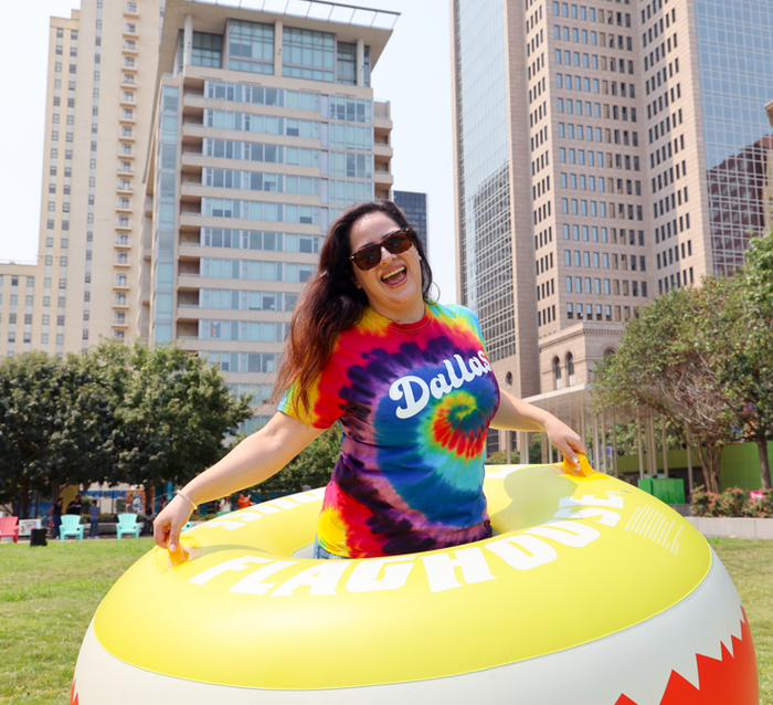 Photo of a woman in sunglasses and the Bullzerk Dallas Script Tie Dye tshirt standing in an inflatable tube outside.