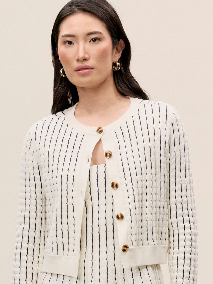 A woman wearing a beige and white striped knit cardigan with scallop rib stitching and a button-front design.