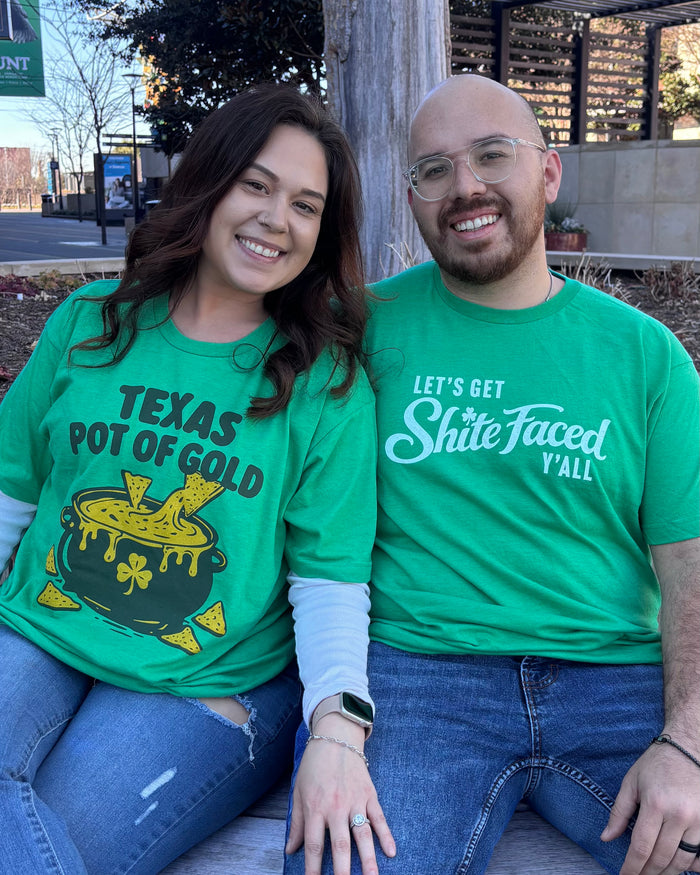 Two people wearing green Bullzerk St. Patrick's Day tshirts with humorous designs, sitting outdoors.