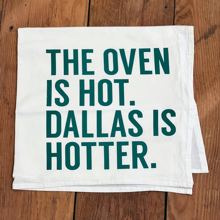 Oven Is Hot Tea Towel featuring the phrase 'THE OVEN IS HOT. DALLAS IS HOTTER.' Perfect for adding a touch of humor to your kitchen, this Texas themed gift makes an ideal souvenir from Texas and is perfect for anyone looking for Texan gifts or a Dallas souvenir.