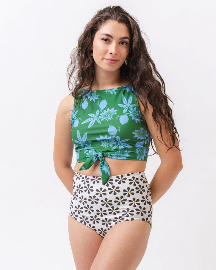 Photo of a woman wearing a green and blue floral/ white and black floral reversible swim bottom (white and black floral side) and a green and blue floral swim crop top