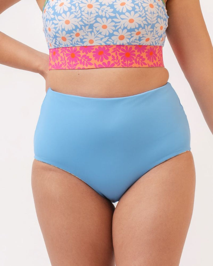 Close up photo of a woman wearing a blue and pink floral cropped swim top with blue high waist reversible swim bottoms
