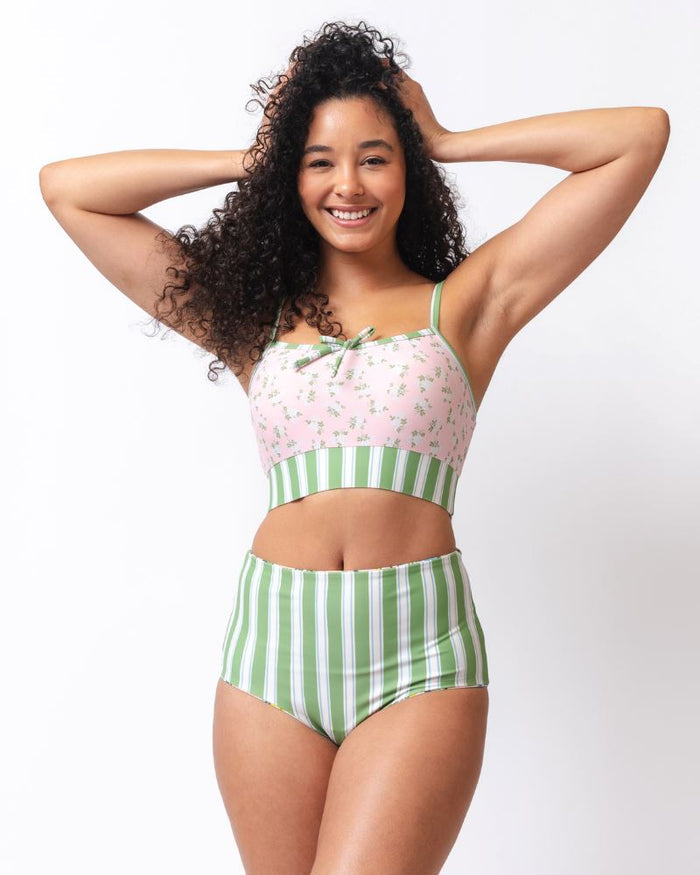 Photo of a woman wearing a pink and green floral swim bralette and a white and pink floral/ green striped reversible swim bottom- striped side