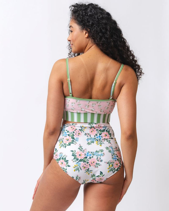 Photo of a woman wearing a pink and green floral swim bralette and a white and pink floral/ green striped reversible swim bottom- floral side- back angle