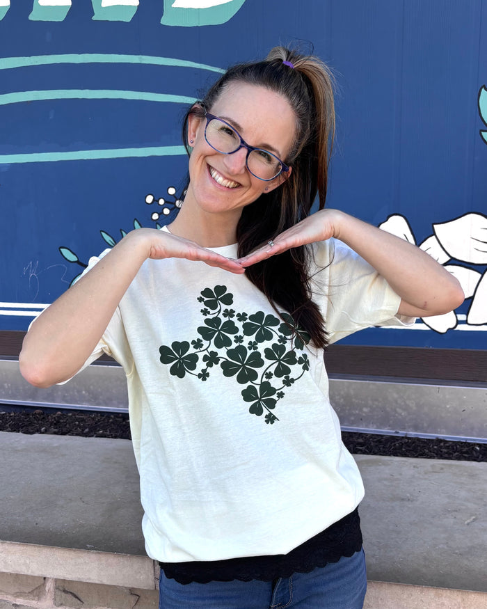 Woman wearing a Bullzerk "Shamrocks Texas" t-shirt and glasses, standing outside and posing in front of a blue mural.