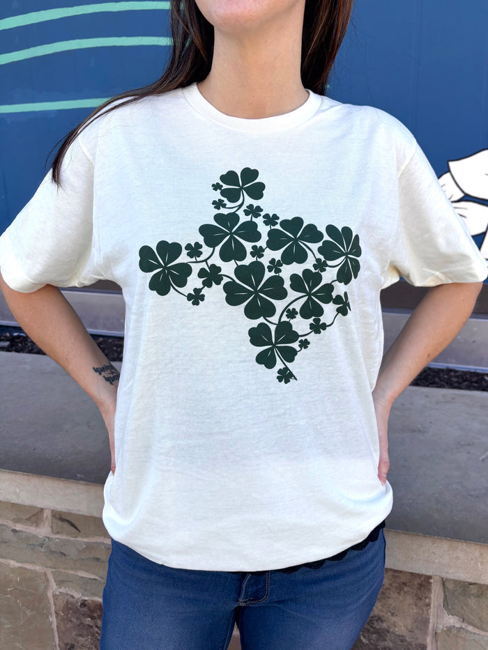 Person wearing a cr\eam tshirt with graphic design of the shape of Texas filled with green shamrocks.