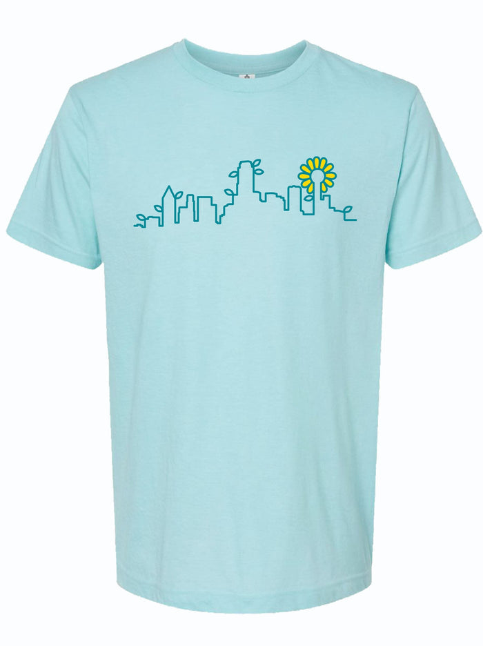 Light blue tshirt with a line-work design of the skyline of Dallas and leaves and a flower on the buildings.