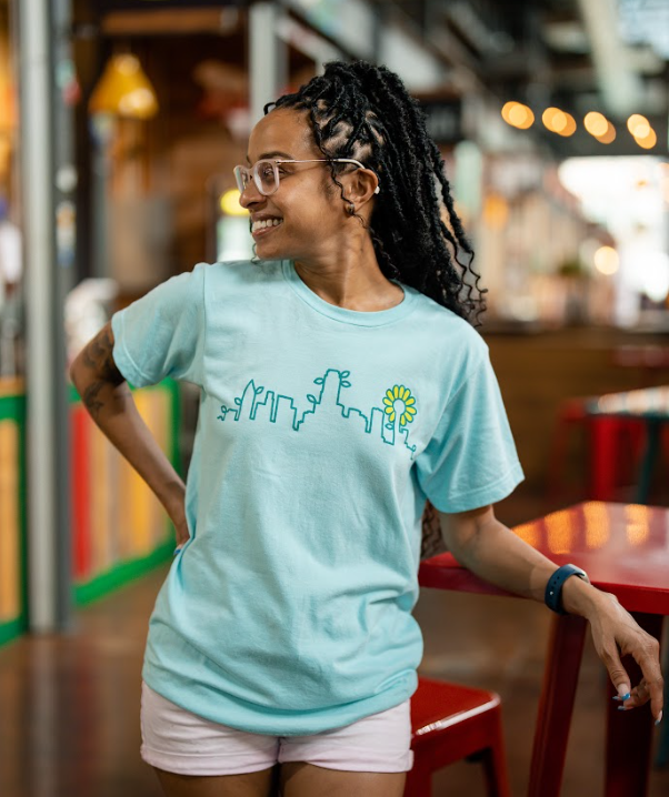 Woman wearing a Bullzerk Skyline Plant tshirt, leaning on a table at the farmers market.