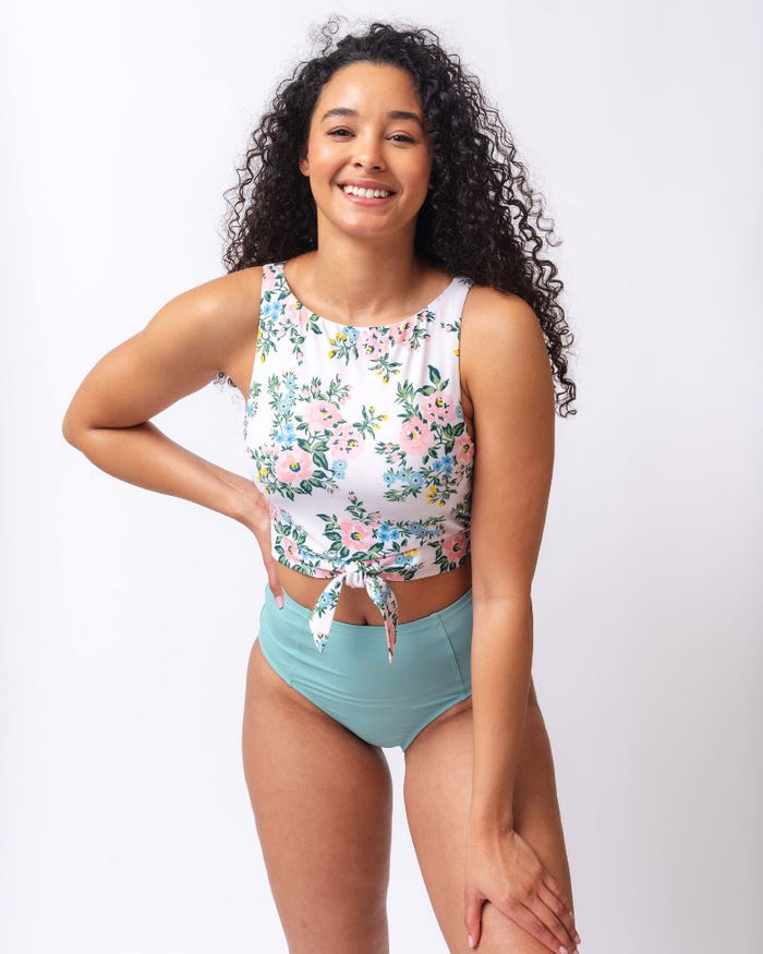 Photo of a woman wearing a pink and white floral cropped swim top with light blue high waist swim bottoms