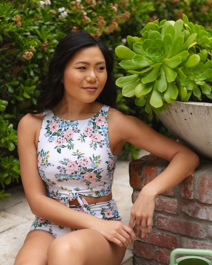 Photo of a woman sitting while wearing a pink and white floral cropped swim top with pink and white floral high waist swim bottoms