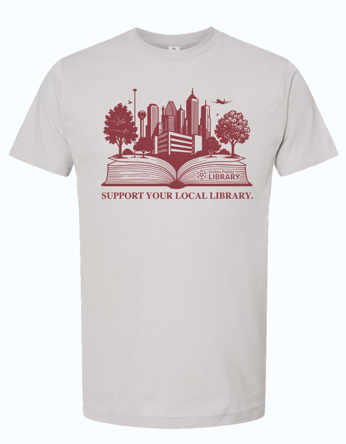 Silver gray tshirt with graphic design of a book laid open with the dallas skyline coming out of it and text underneath reading "Support your local library" in maroon ink.