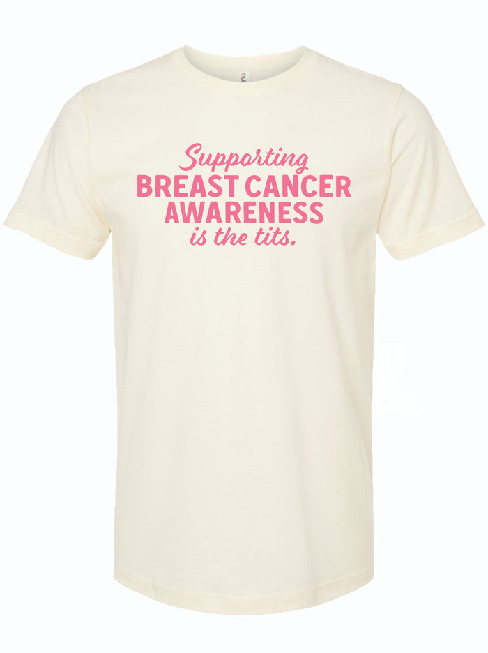 A unisex fine jersey tee in cream color featuring the text 'Supporting Breast Cancer Awareness is the tits.' This stylish shirt is a great Texas themed gift, perfect for raising awareness and making a statement. A fantastic choice among Texas Made Gifts and ideal souvenirs from Texas, this shirt also makes for a unique Dallas souvenir or a special treat in the realm of Texan gifts.