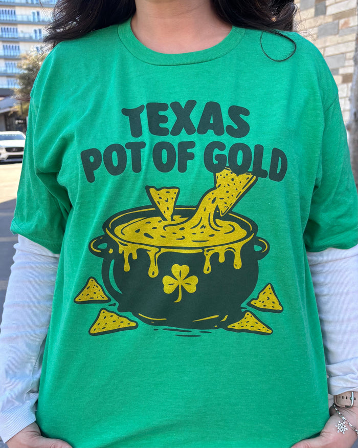 Person wearing a green tshirt with graphic design of a pot of queso with chips, underneath text reading "Texas Pot of gold" In dark green letters.