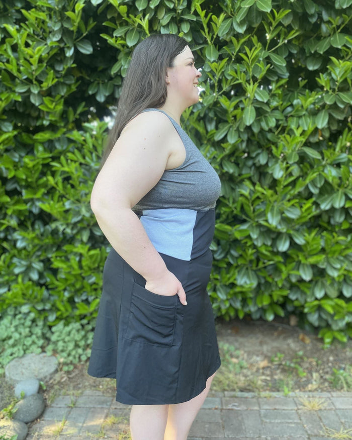 Person wearing a gray dress against a green hedge background looking sideways