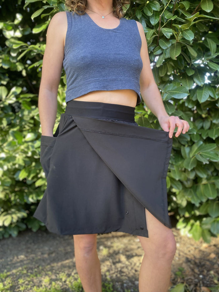 Person wearing a blue sleeveless top and black skirt against a green hedge background