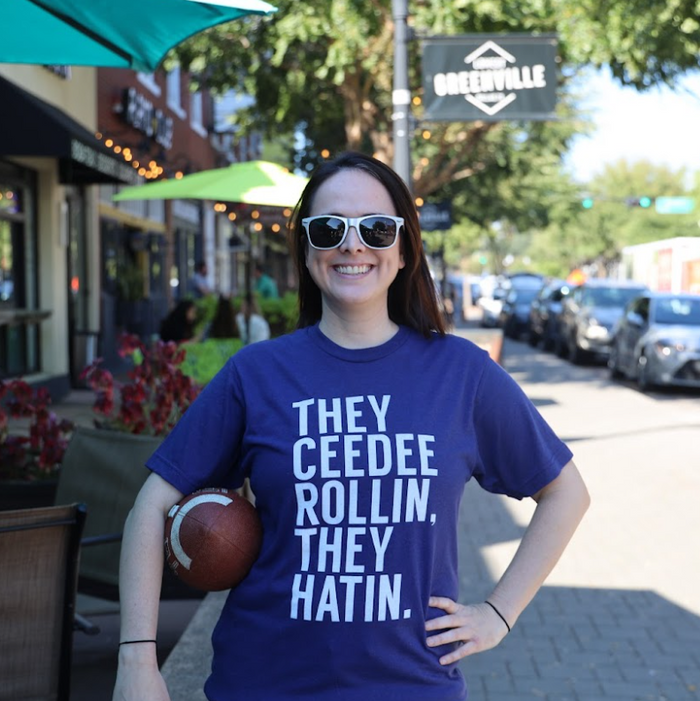 Woman wearing a Bullzerk Ceedee Rollin t-shirt, standing on a street with storefronts and cars in the background.
