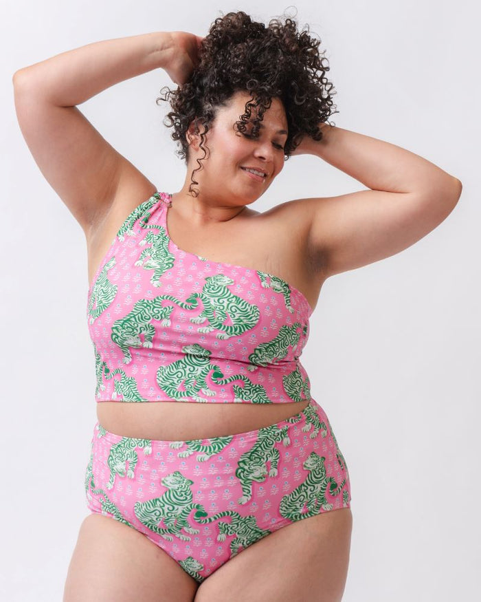 Photo of a woman wearing a bold pink and green tiger print one shoulder crop swim top with matching high waist swim bottoms